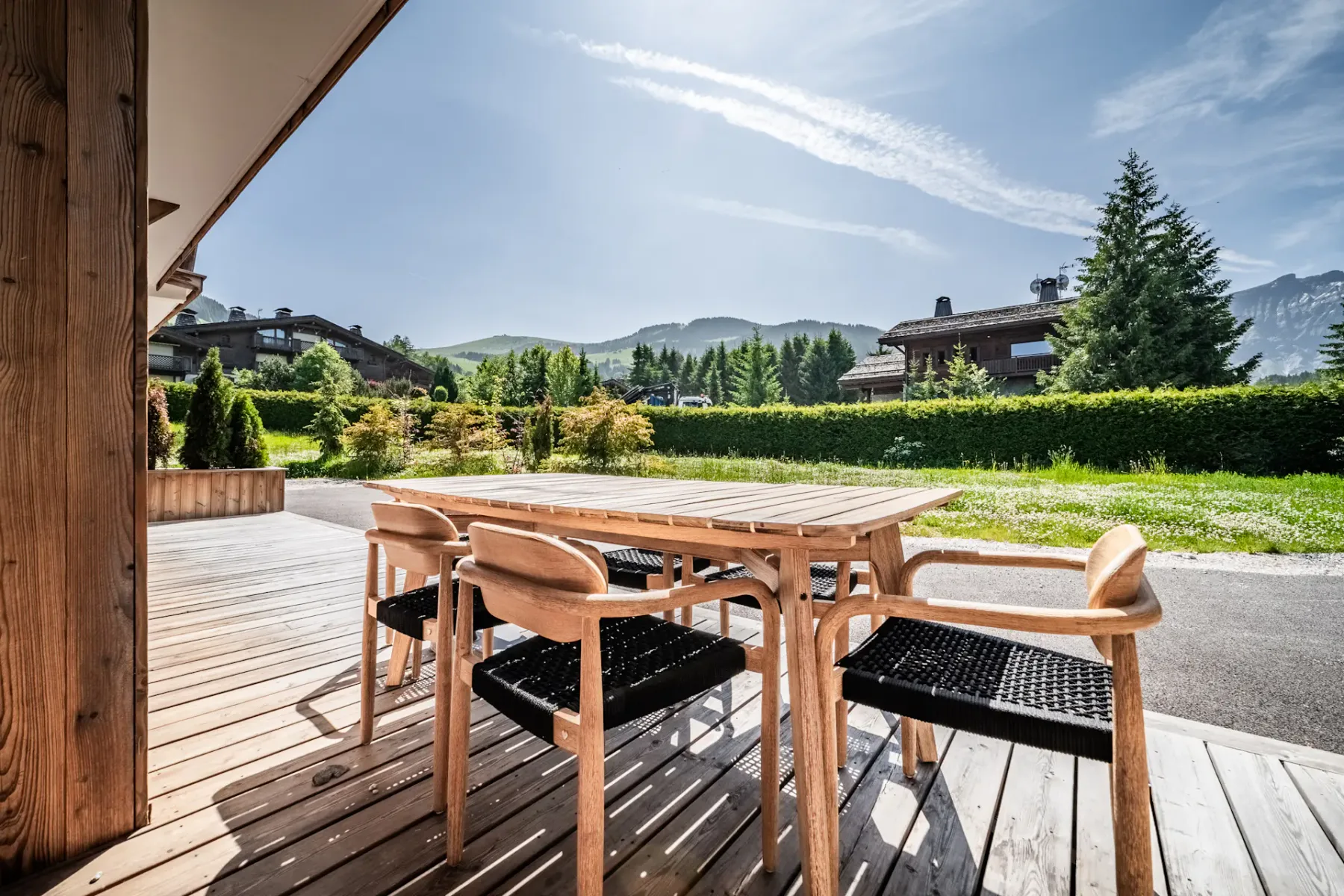 Una zona de comedor al aire libre en una terraza de madera tiene vistas a jardines y montañas lejanas.