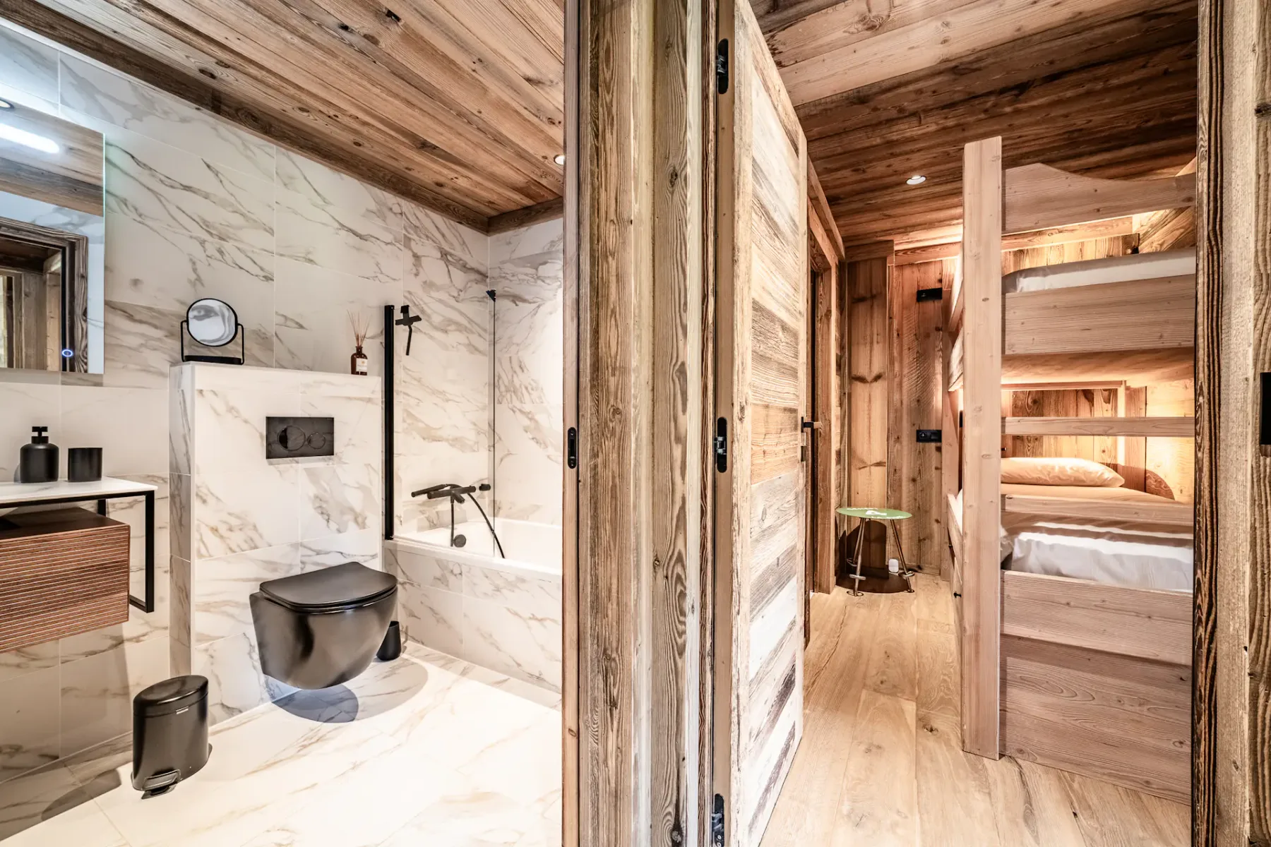 Un baño de mármol con un inodoro negro está junto a una zona para dormir revestida de madera.