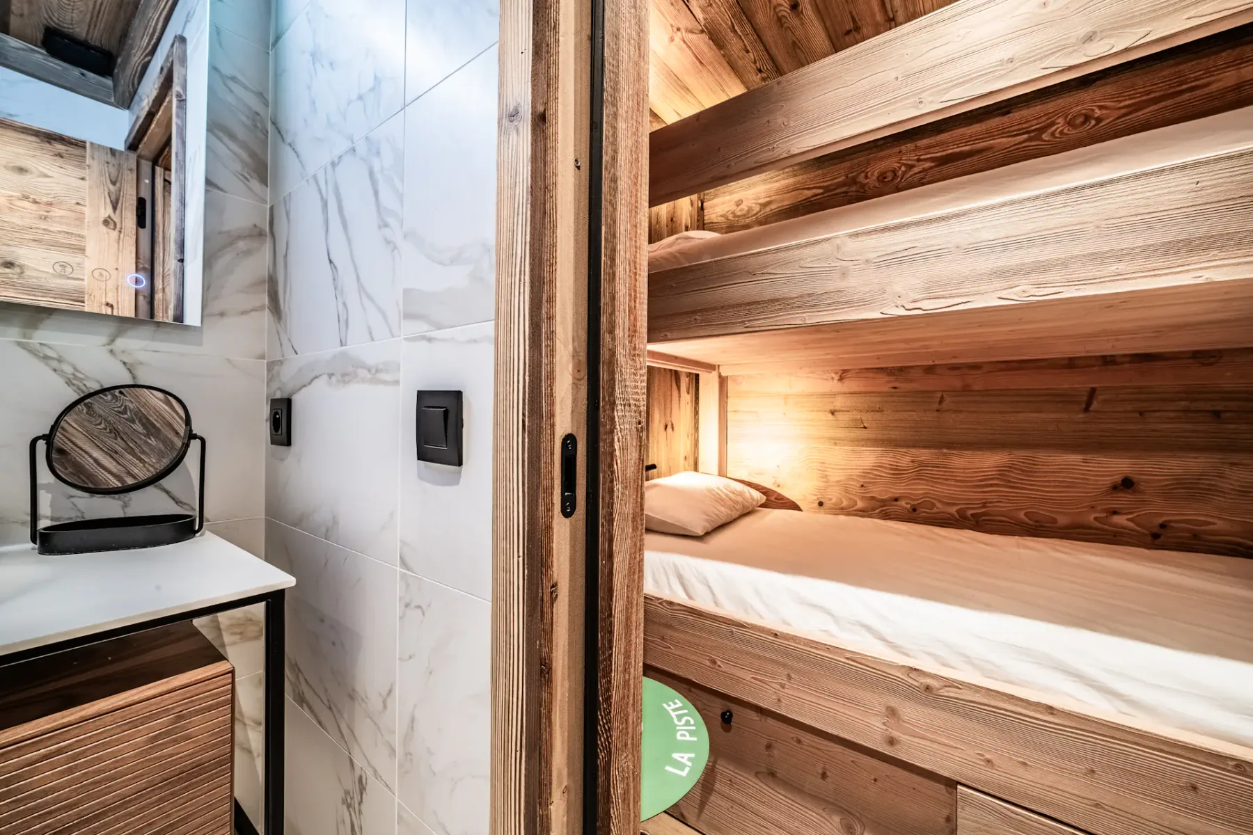 Un dormitorio compacto con literas de madera junto a una zona de lavado revestida de azulejos.