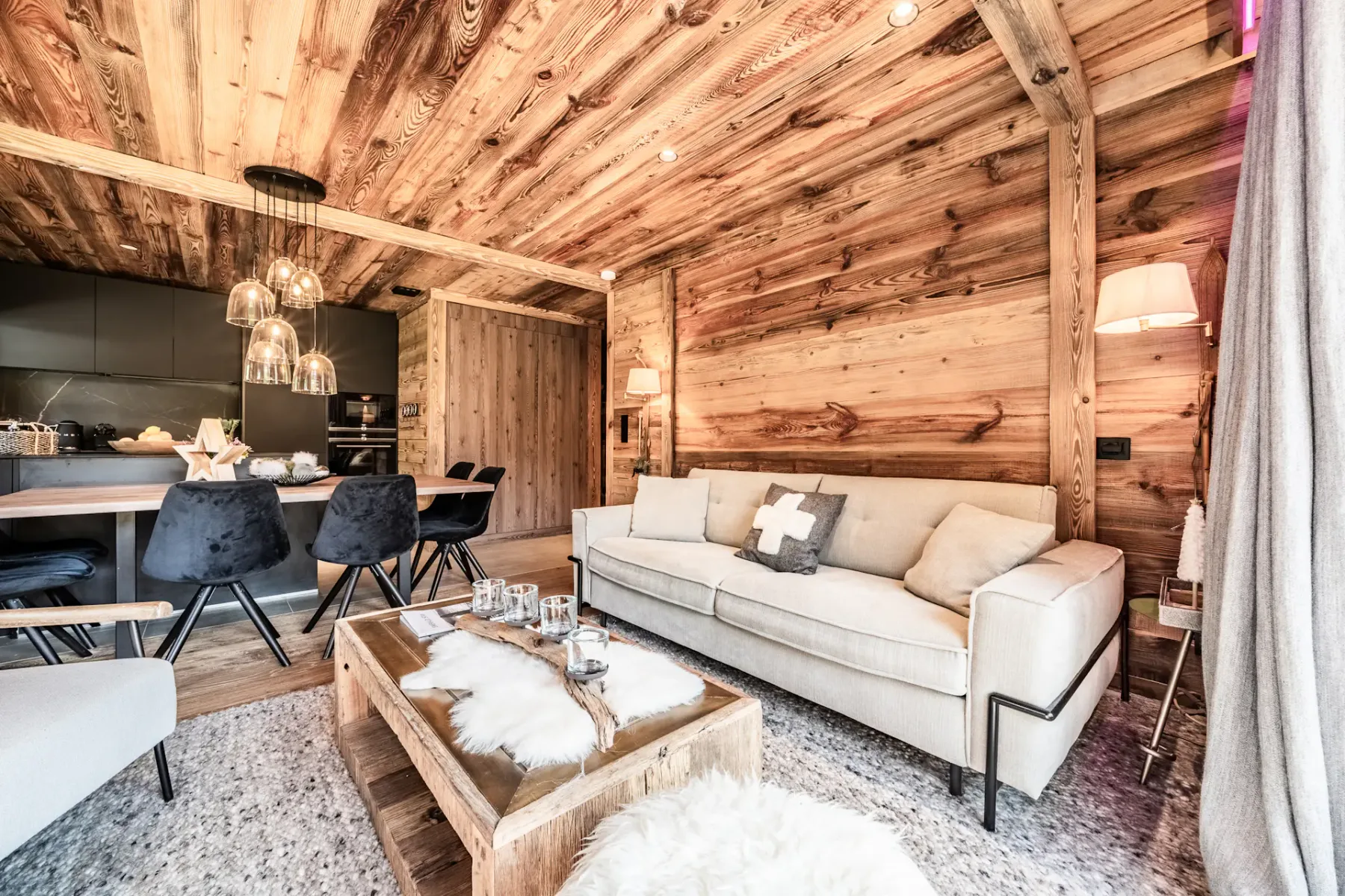 Una sala de estar con paneles de madera, un sofá claro y un comedor abierto.