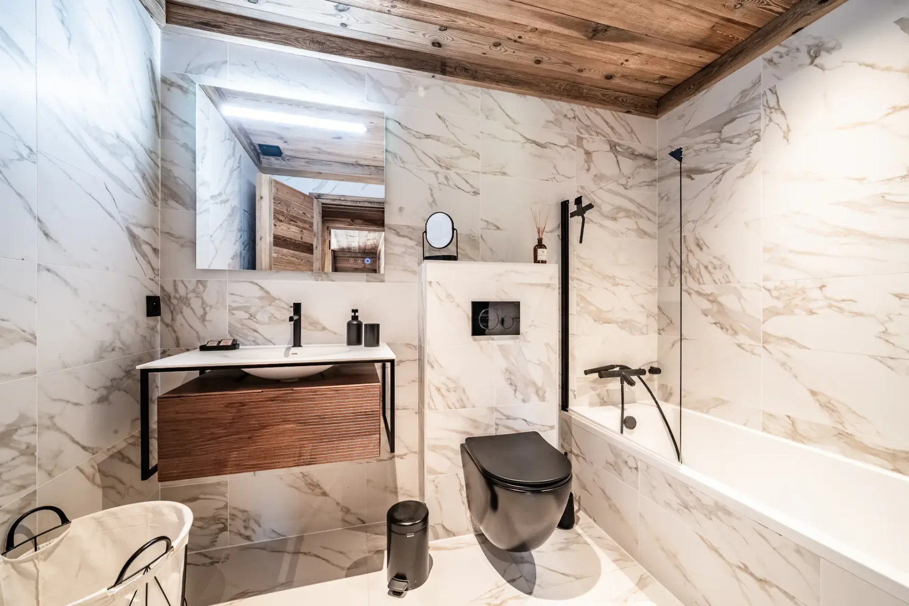 Baño con revestimiento de mármol, mueble suspendido y bañera con ducha.