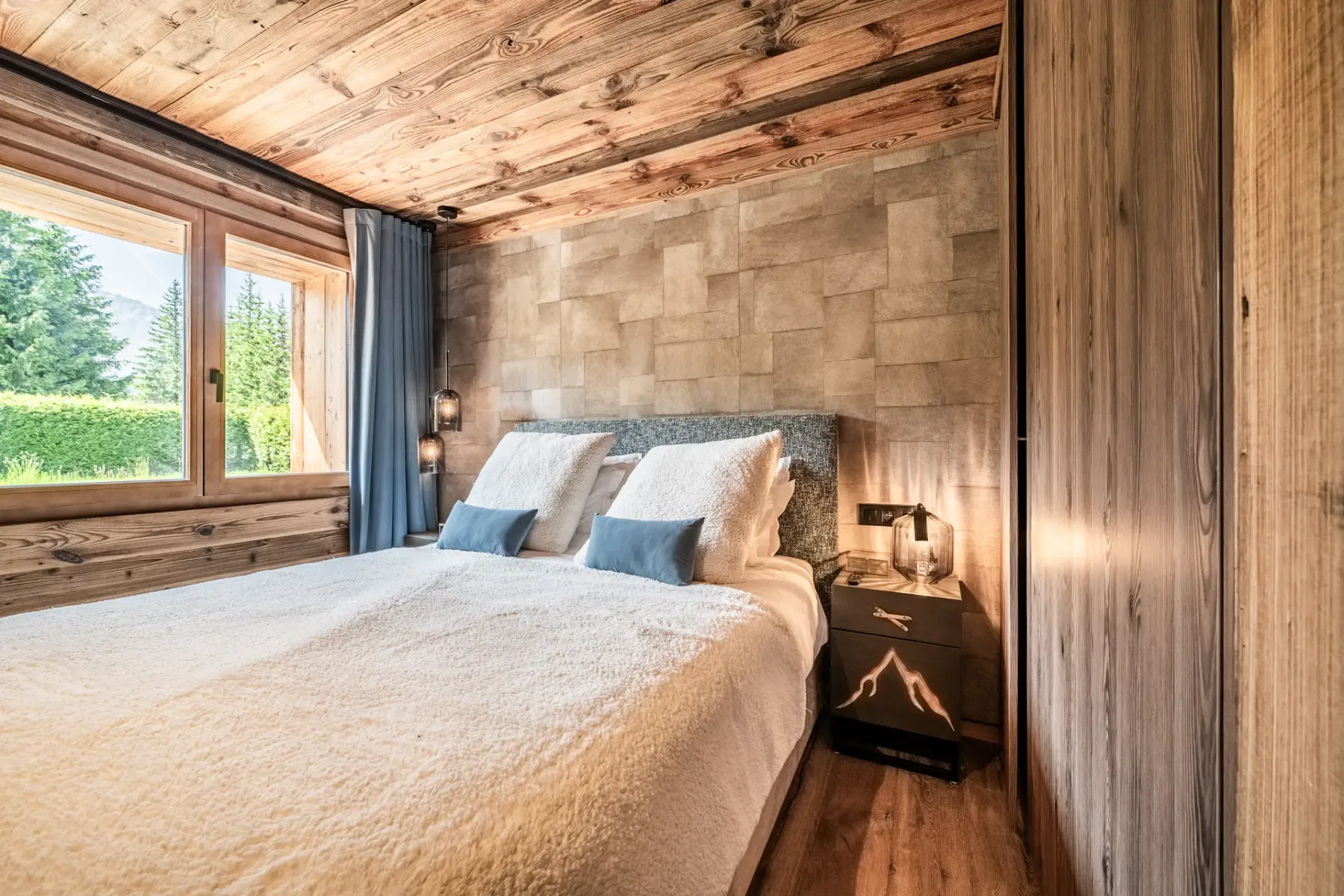 Un dormitorio con ropa de cama blanca, cojines azules y una ventana junto a la cama.