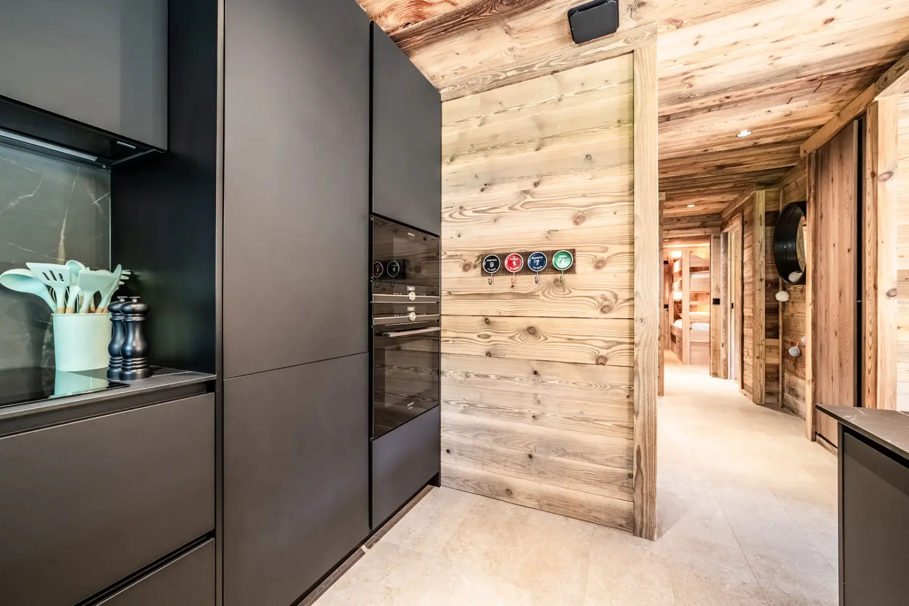 Una cocina moderna con armarios oscuros da a un pasillo revestido de madera.