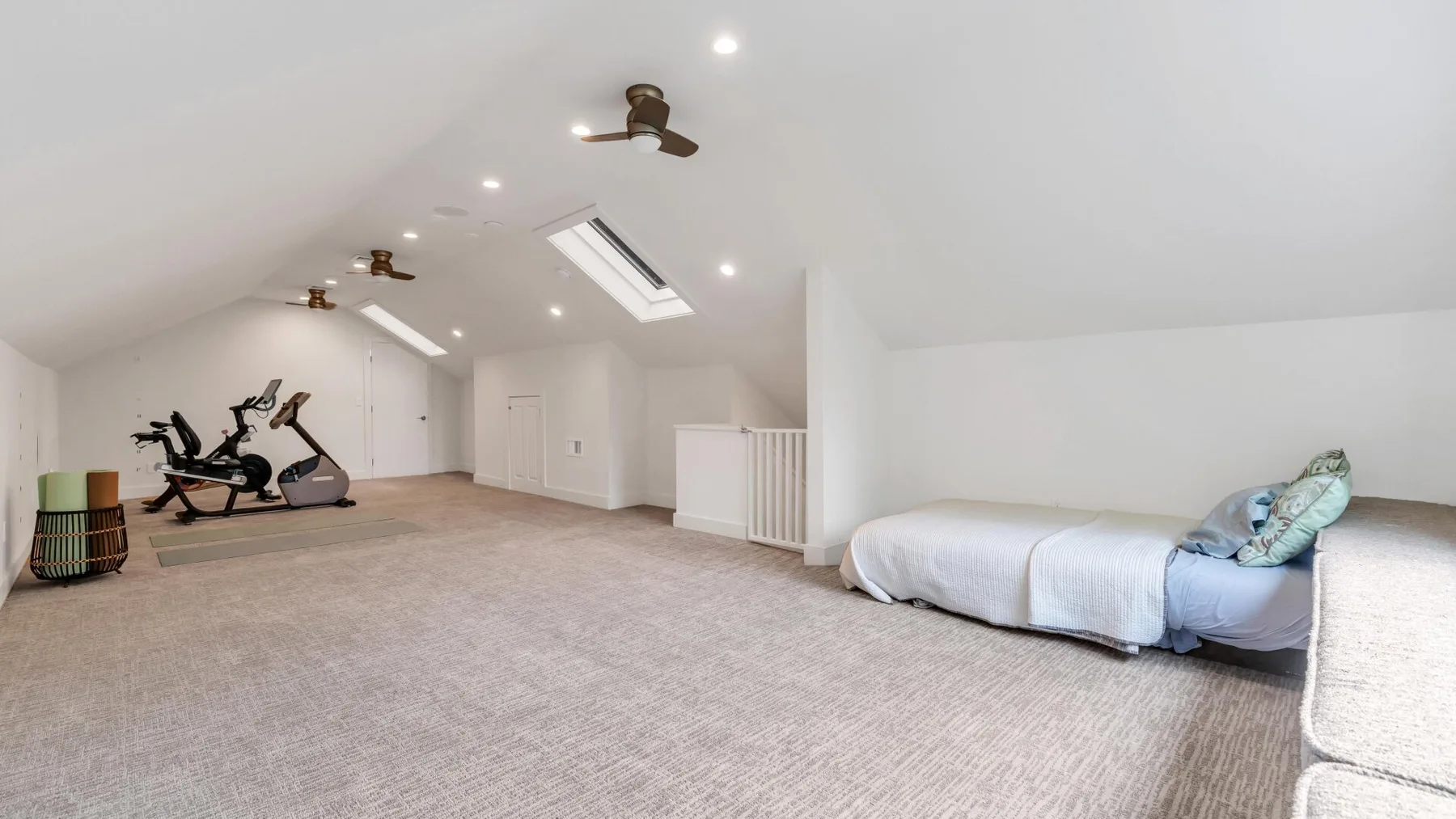 A carpeted attic room with exercise equipment and a low bed.