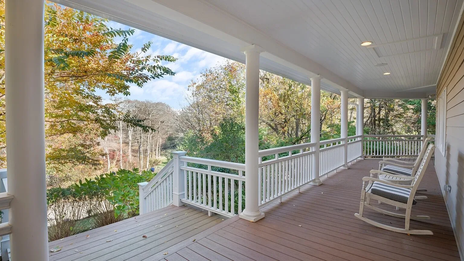 A covered porch with white railings and trees visible beyond it.