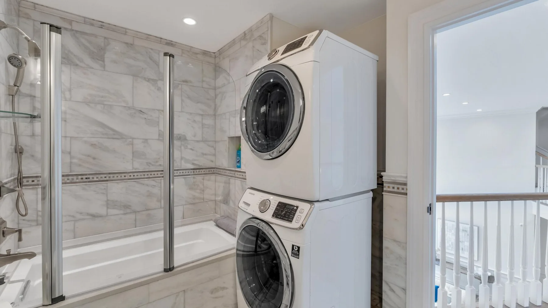 A tiled bathroom with a glass shower and stacked laundry machines.