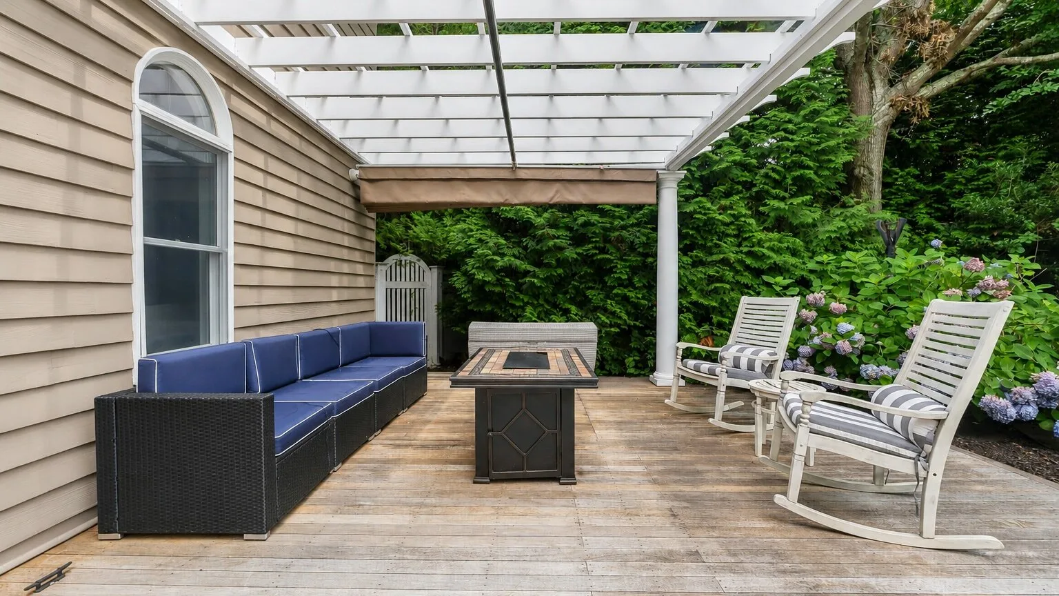 A covered outdoor deck with cushioned seating and a wooden table.