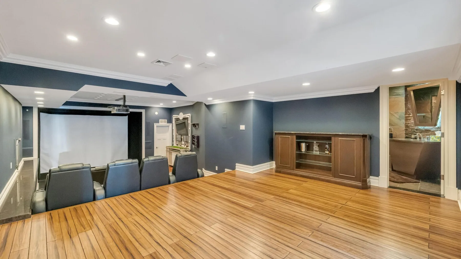 A spacious entertainment room with a large screen, seating, and polished wood flooring.
