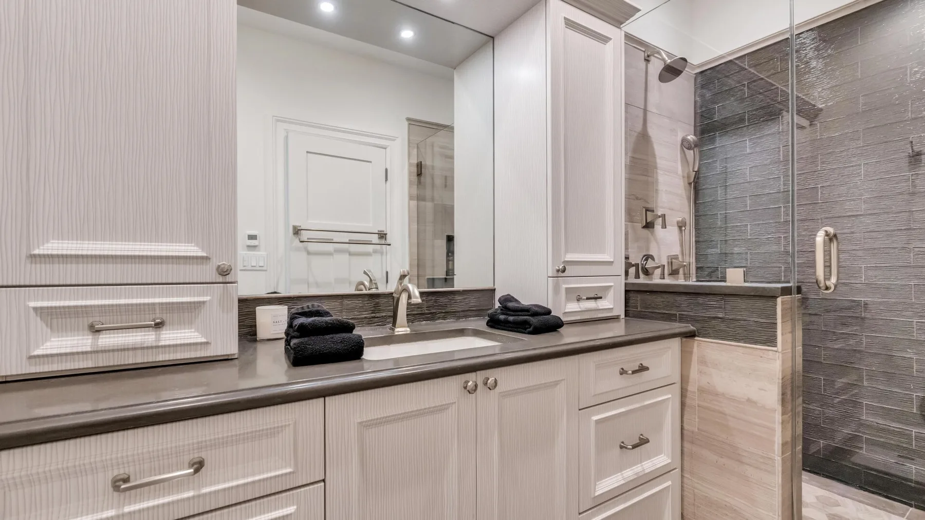 A bathroom vanity with folded towels sits beside a glass-enclosed shower.