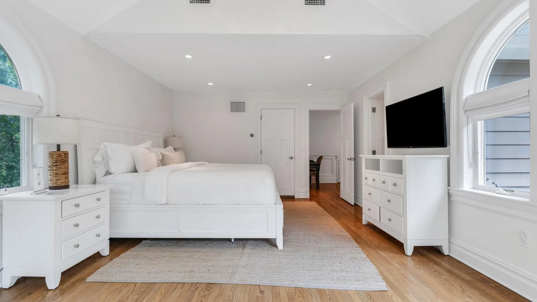 A bright bedroom with a white bed, a large rug, and a television.