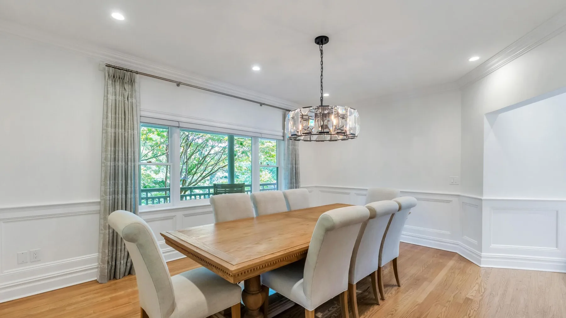 A dining room with a wooden table and upholstered seating beside large windows.