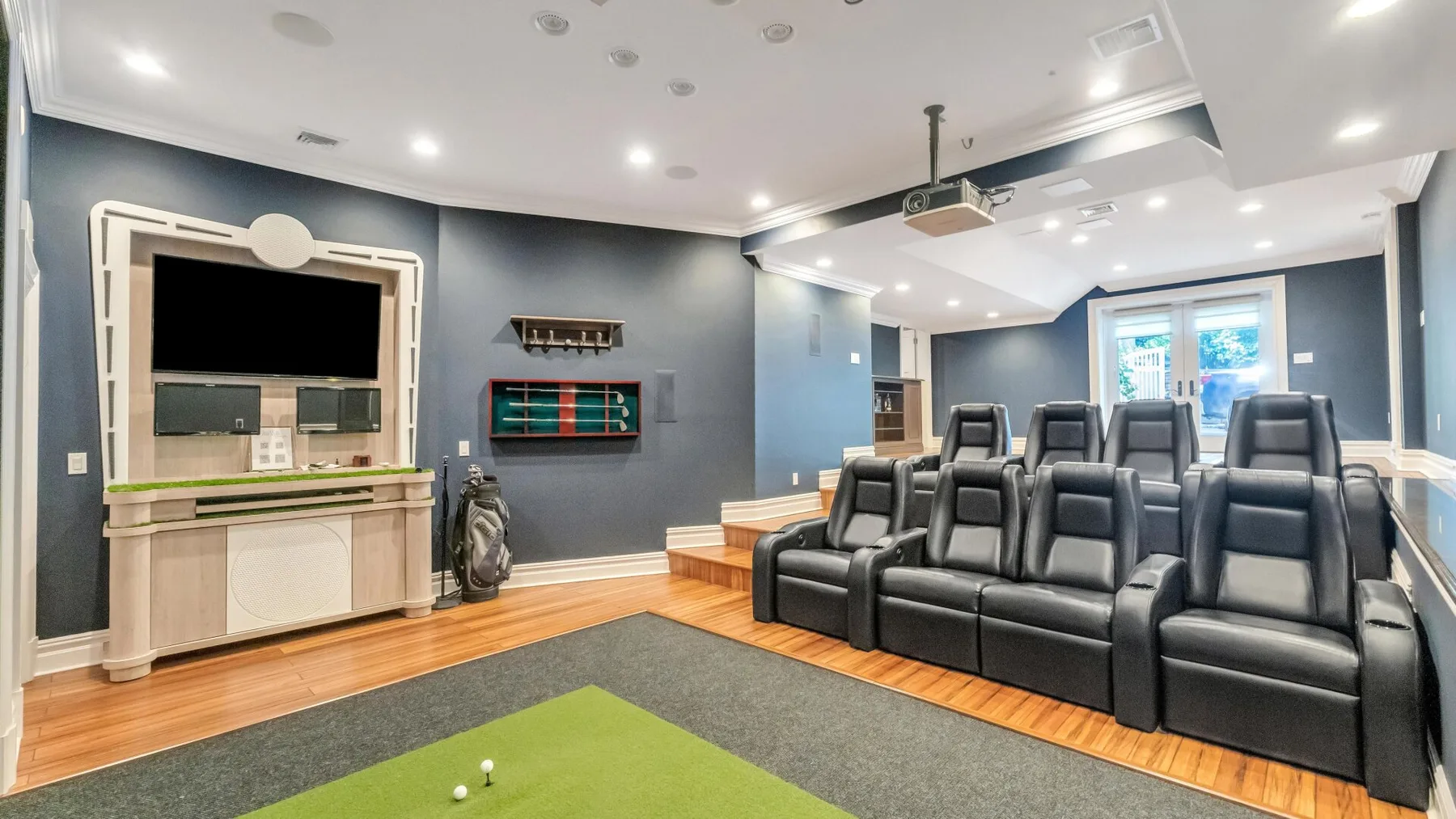 A home theater with rows of dark reclining seats and a green putting mat.