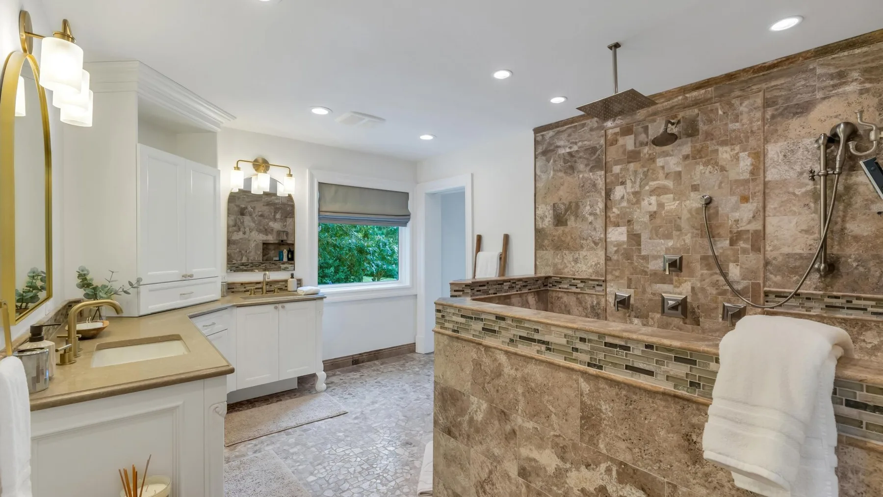 A spacious bathroom with a white vanity, window, and tiled bathtub.