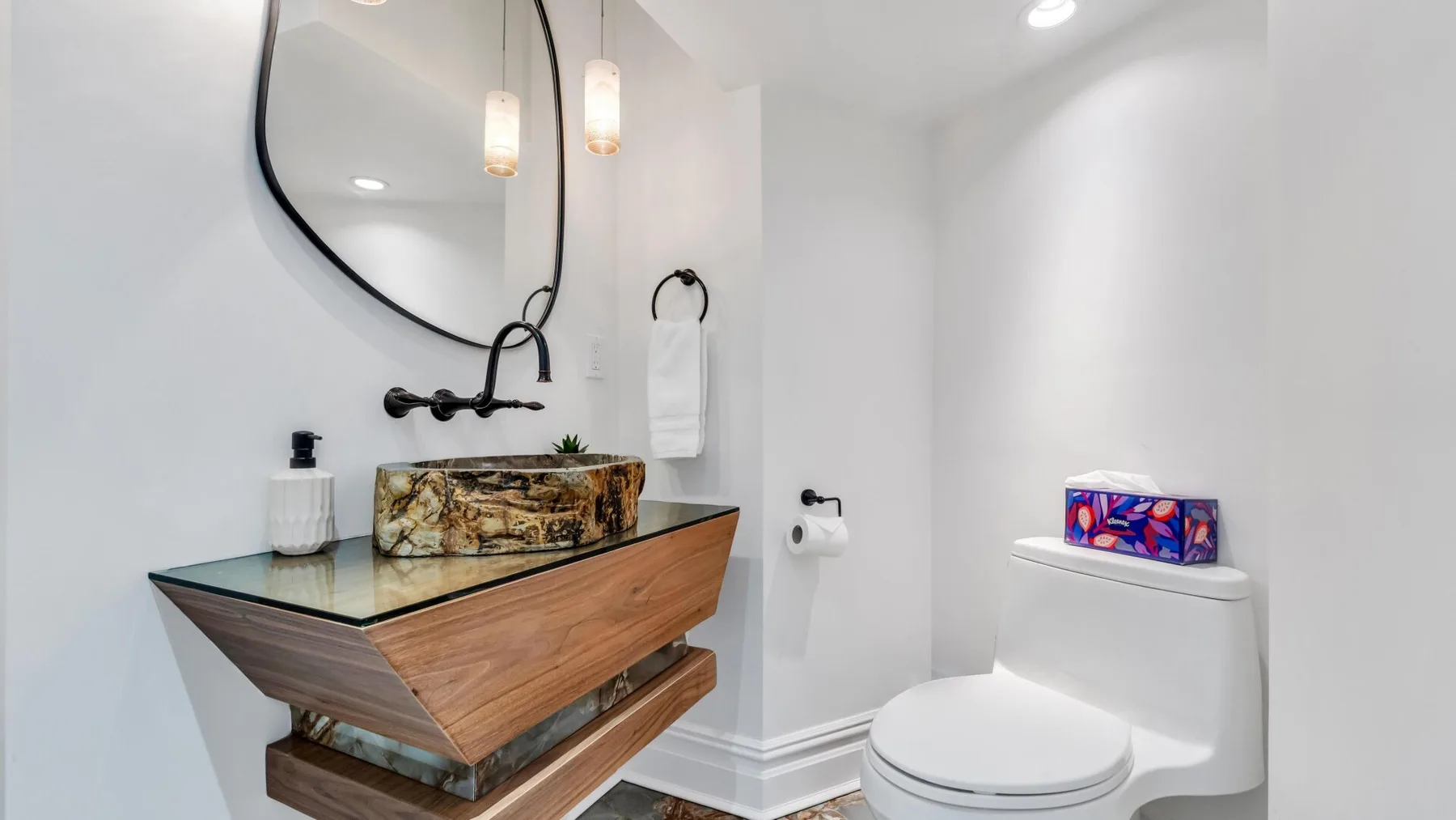 A bright bathroom with a wood-toned vanity, round mirror, and toilet.