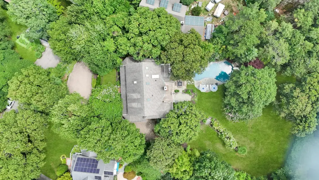 An aerial view shows a house surrounded by trees, lawn, and a small swimming pool.