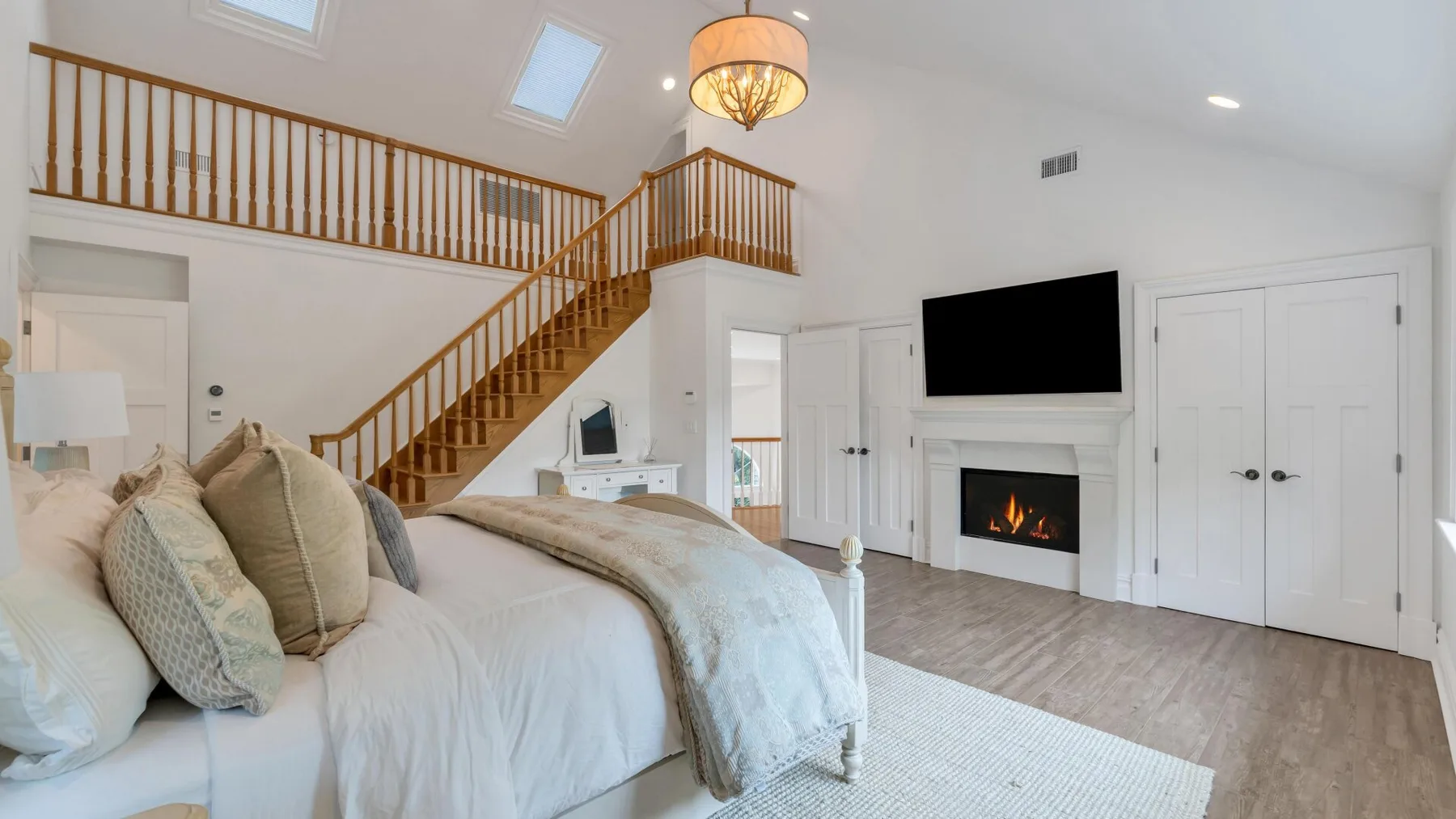 A bedroom with a large bed beneath a wooden staircase and loft railing.