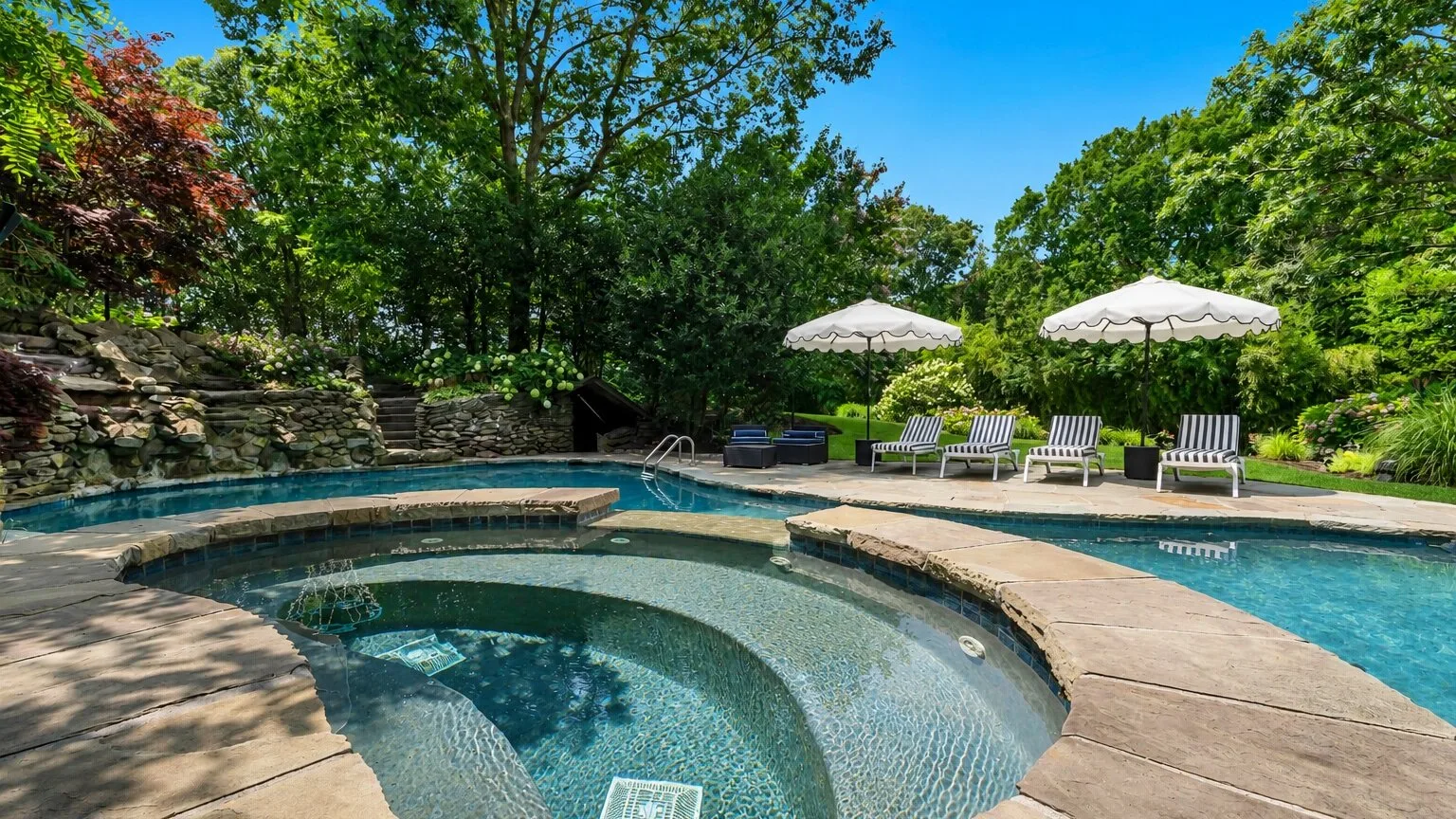 An outdoor swimming pool with curved steps, lounge chairs, and umbrellas.