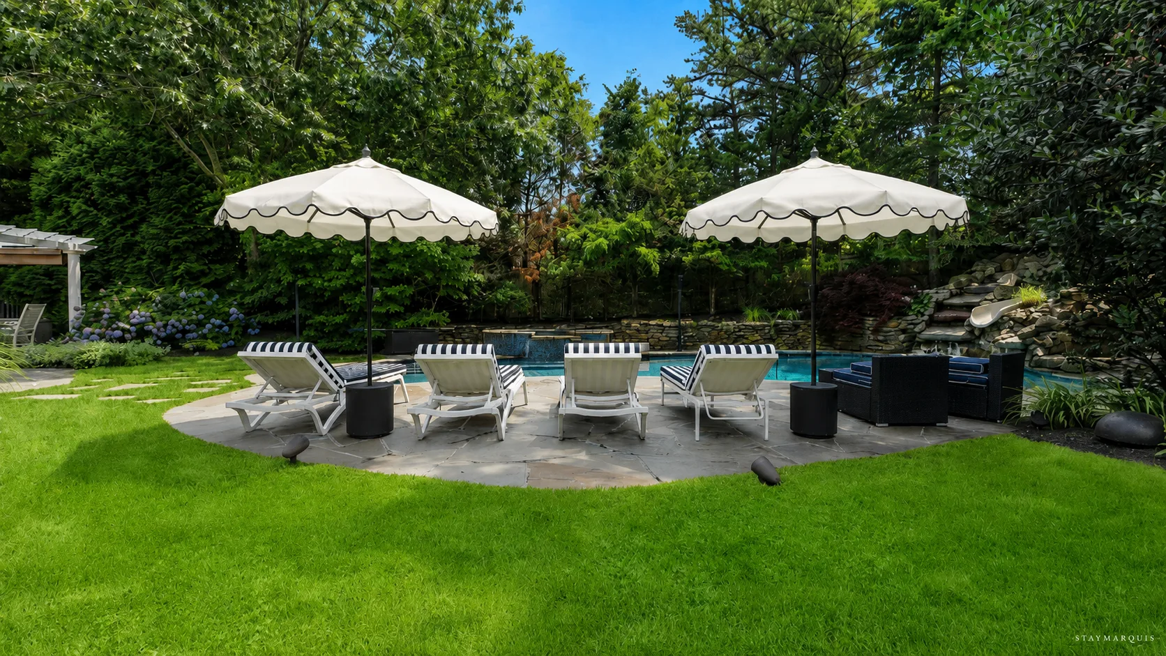 An outdoor patio with lounge seating and umbrellas sits beside a swimming pool.