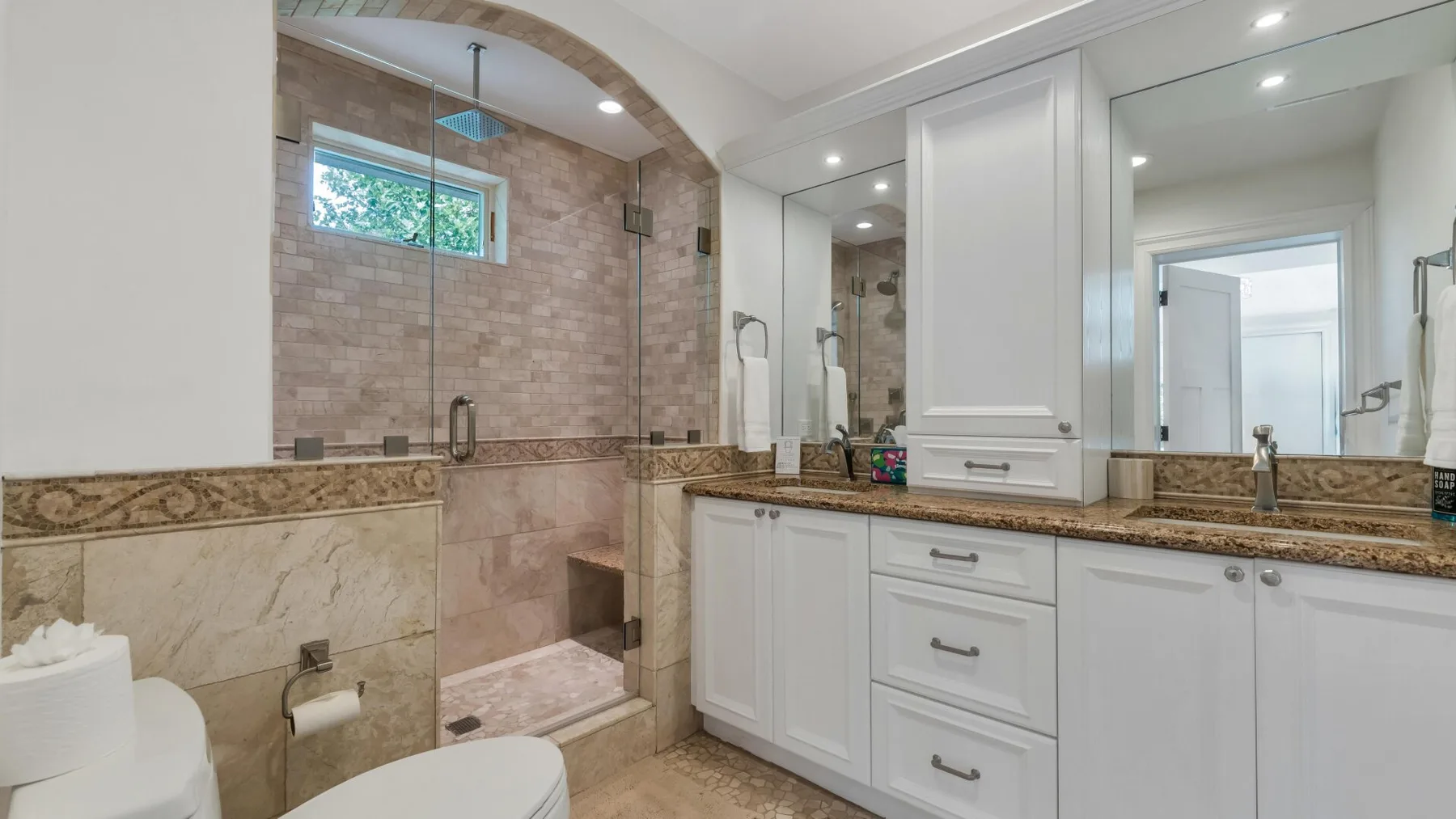 A bathroom with a large vanity, mirrors, and a tiled shower area.