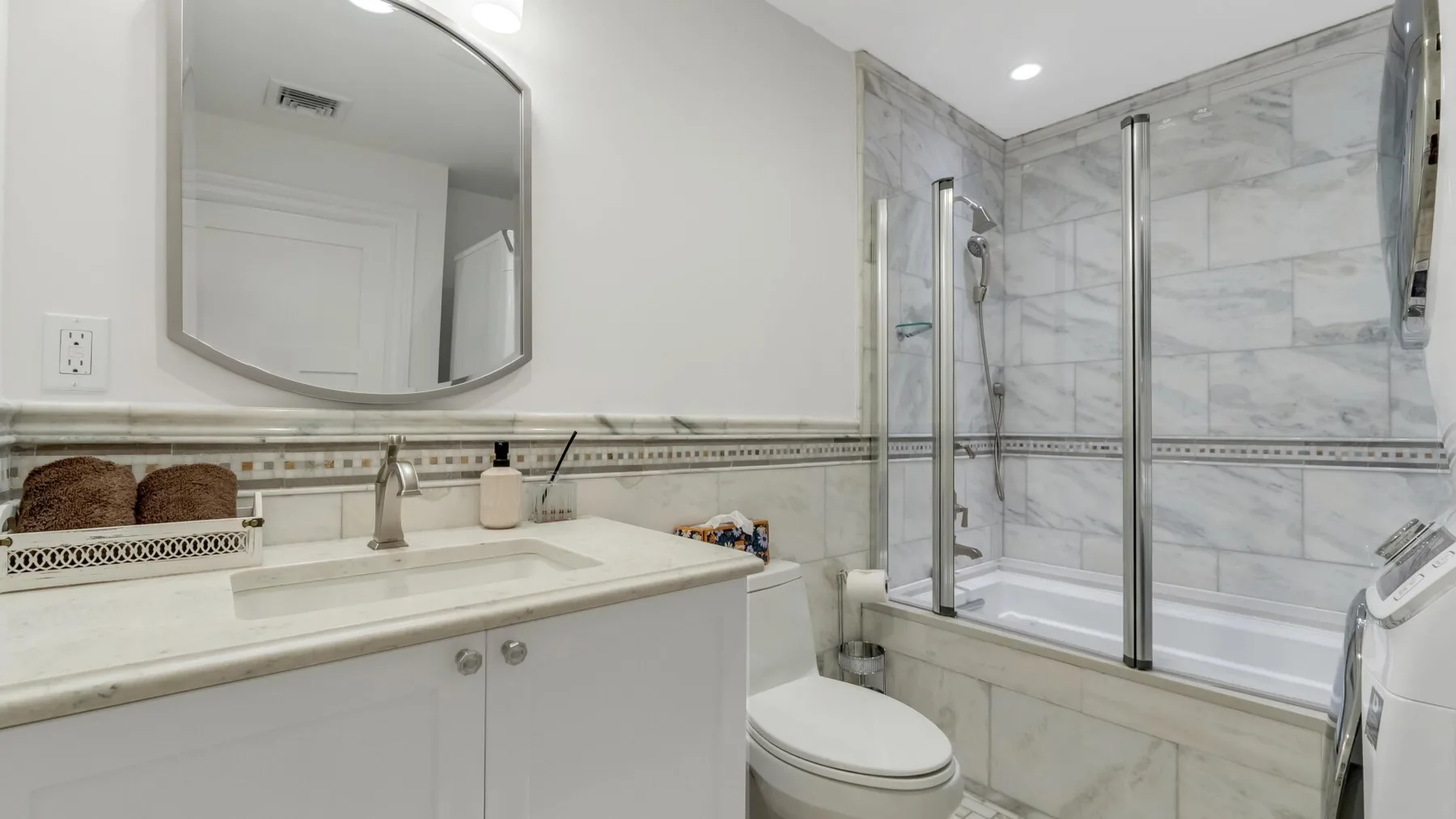 A bathroom with a vanity, toilet, and glass-enclosed bathtub.