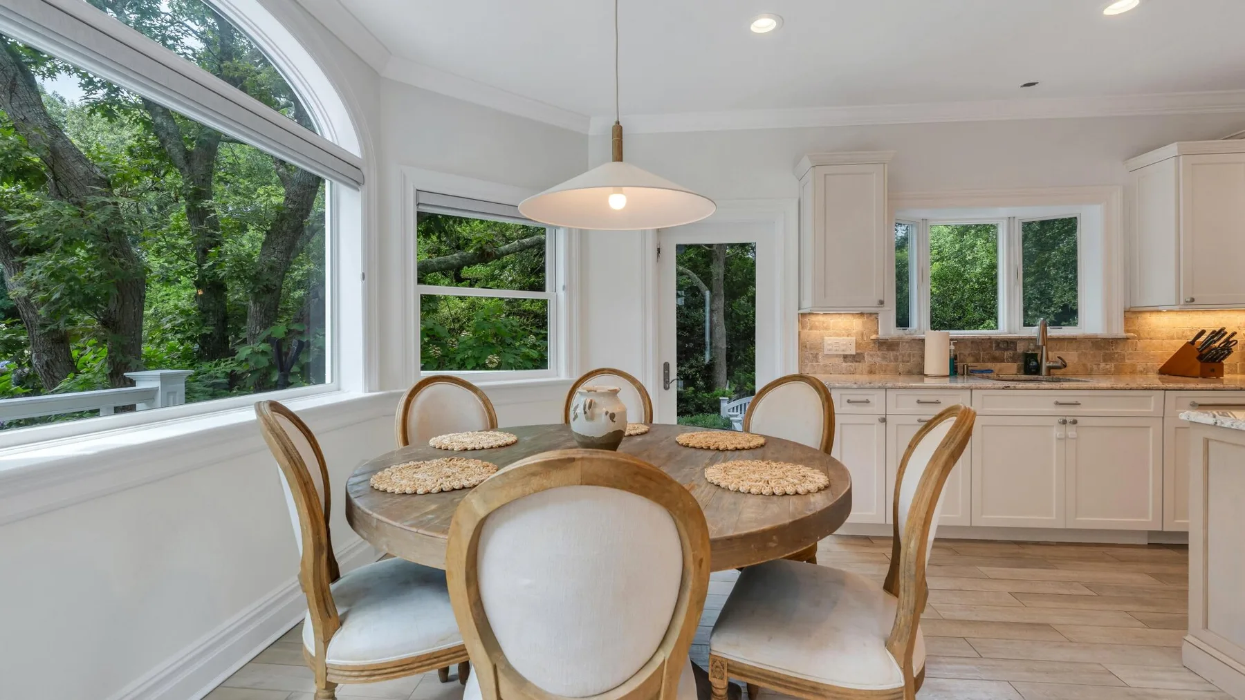 A bright dining area with a round table beside a large arched window.