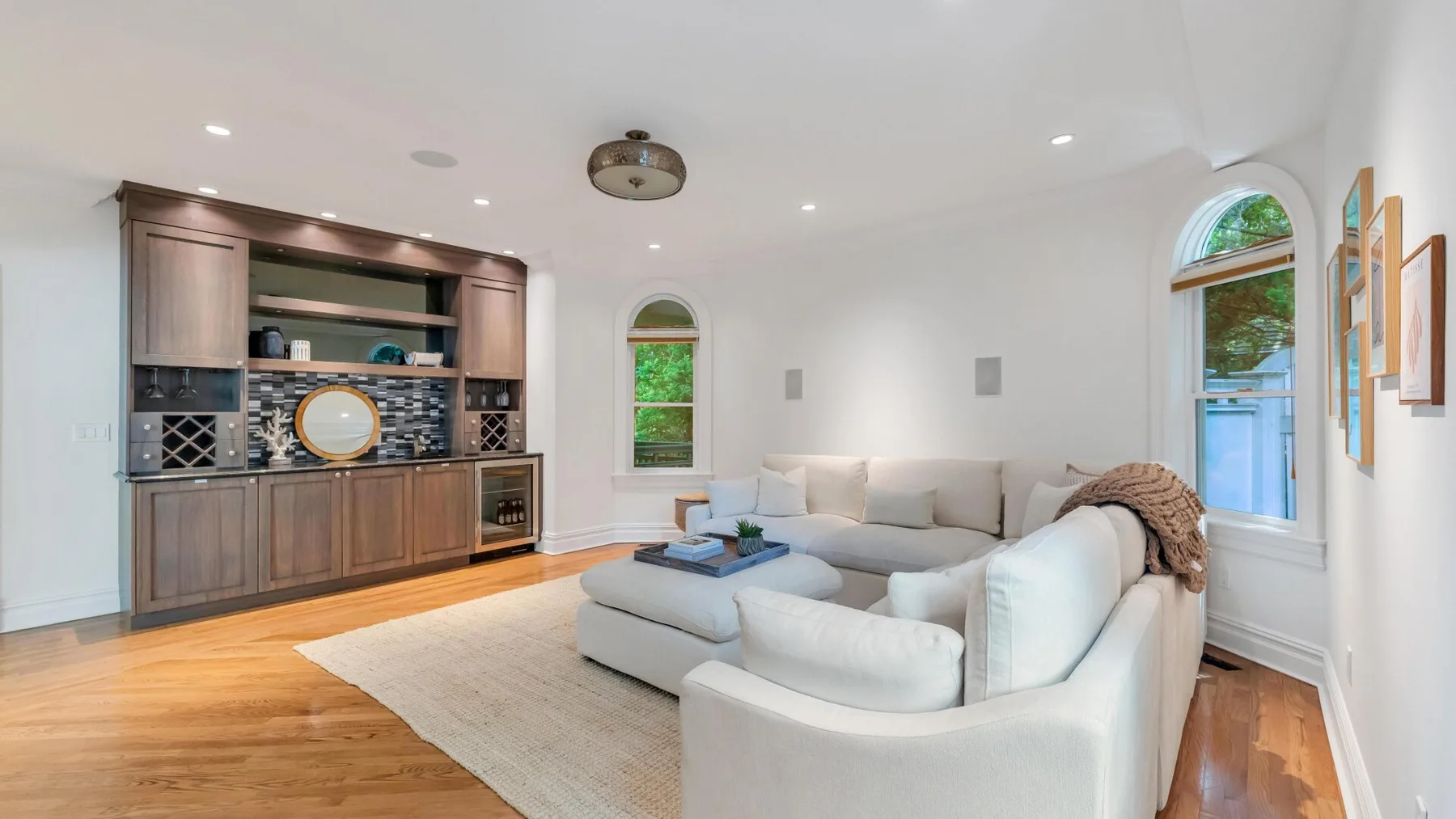 A bright living room with white seating and a built-in bar along the wall.