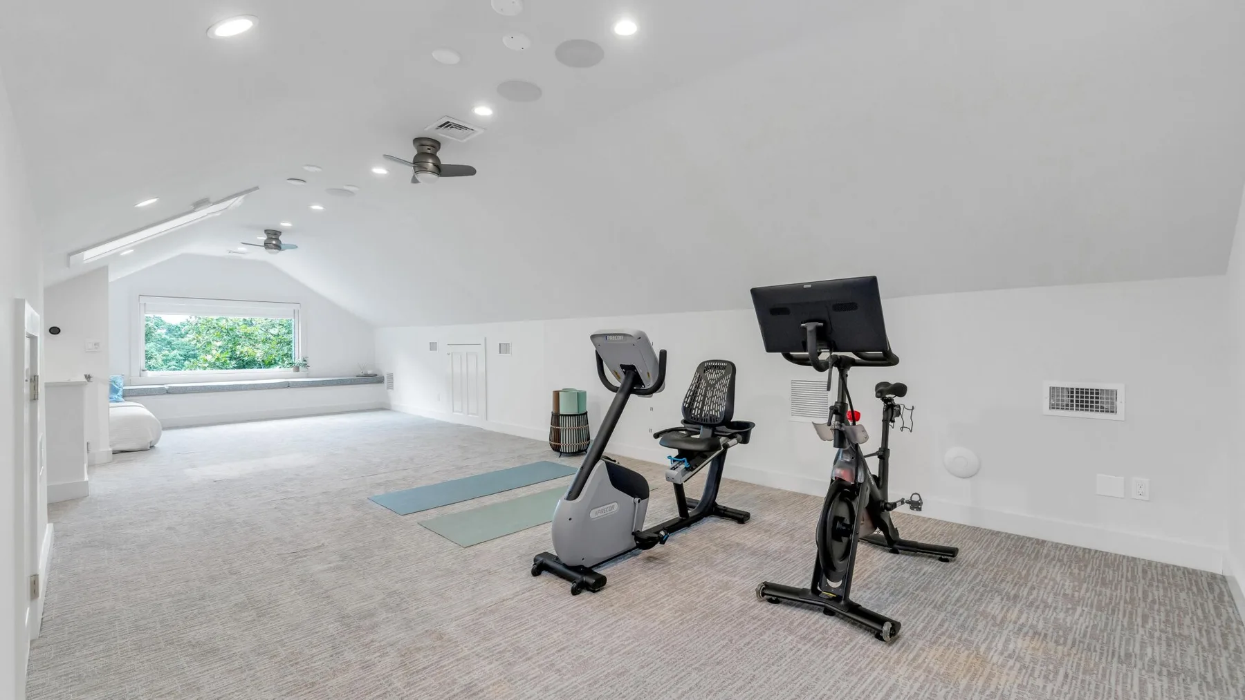 A bright attic exercise room with stationary bikes and a large window.