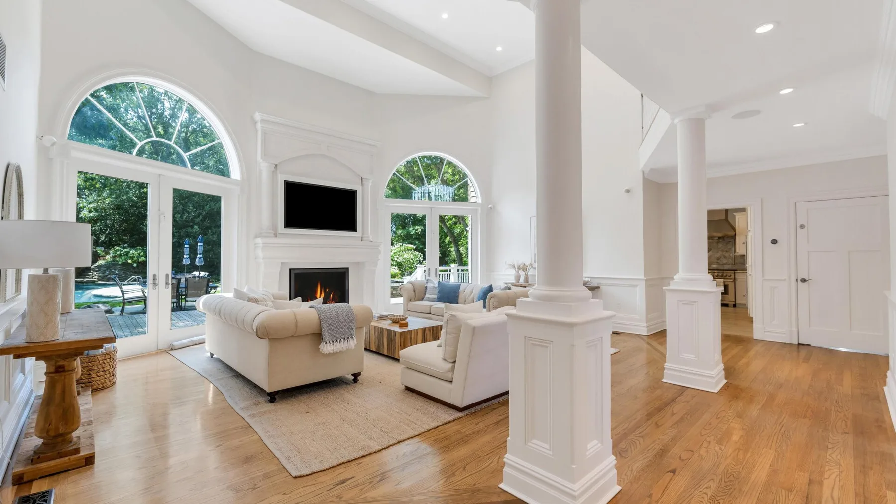 A bright living room with seating around a fireplace and tall arched windows.