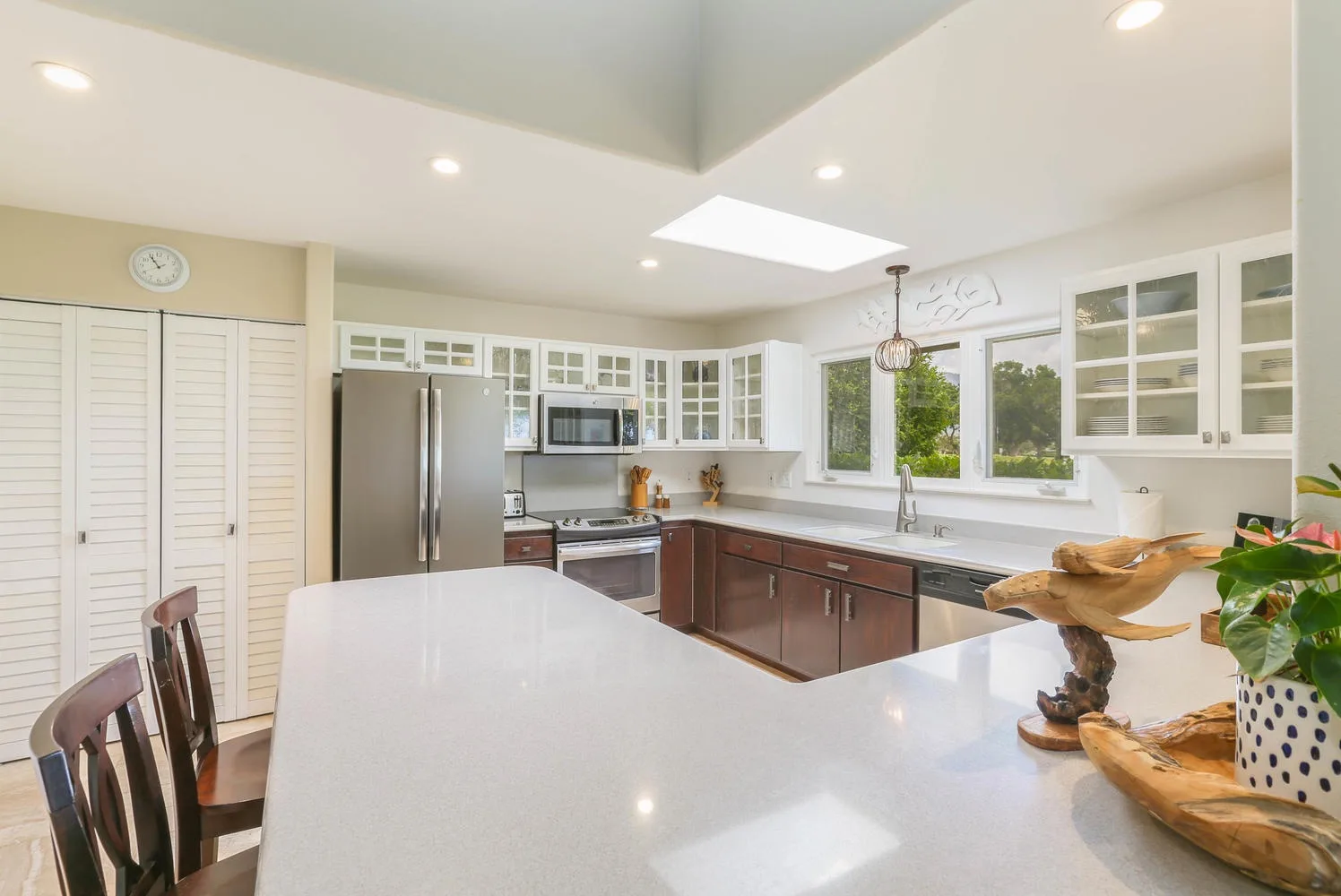 Una cocina luminosa con una isla grande, gabinetes oscuros y electrodomésticos de acero inoxidable.