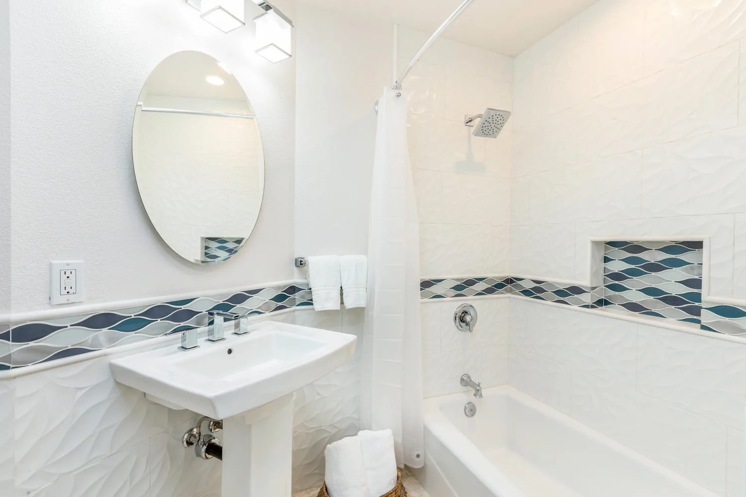 Un baño luminoso con lavabo, espejo ovalado y bañera con ducha.