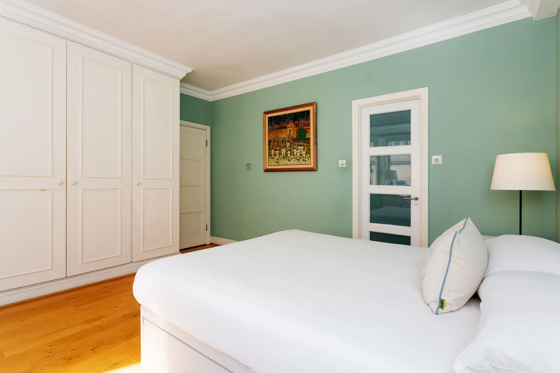 A bedroom with a large bed, built-in wardrobes, and a framed wall picture.