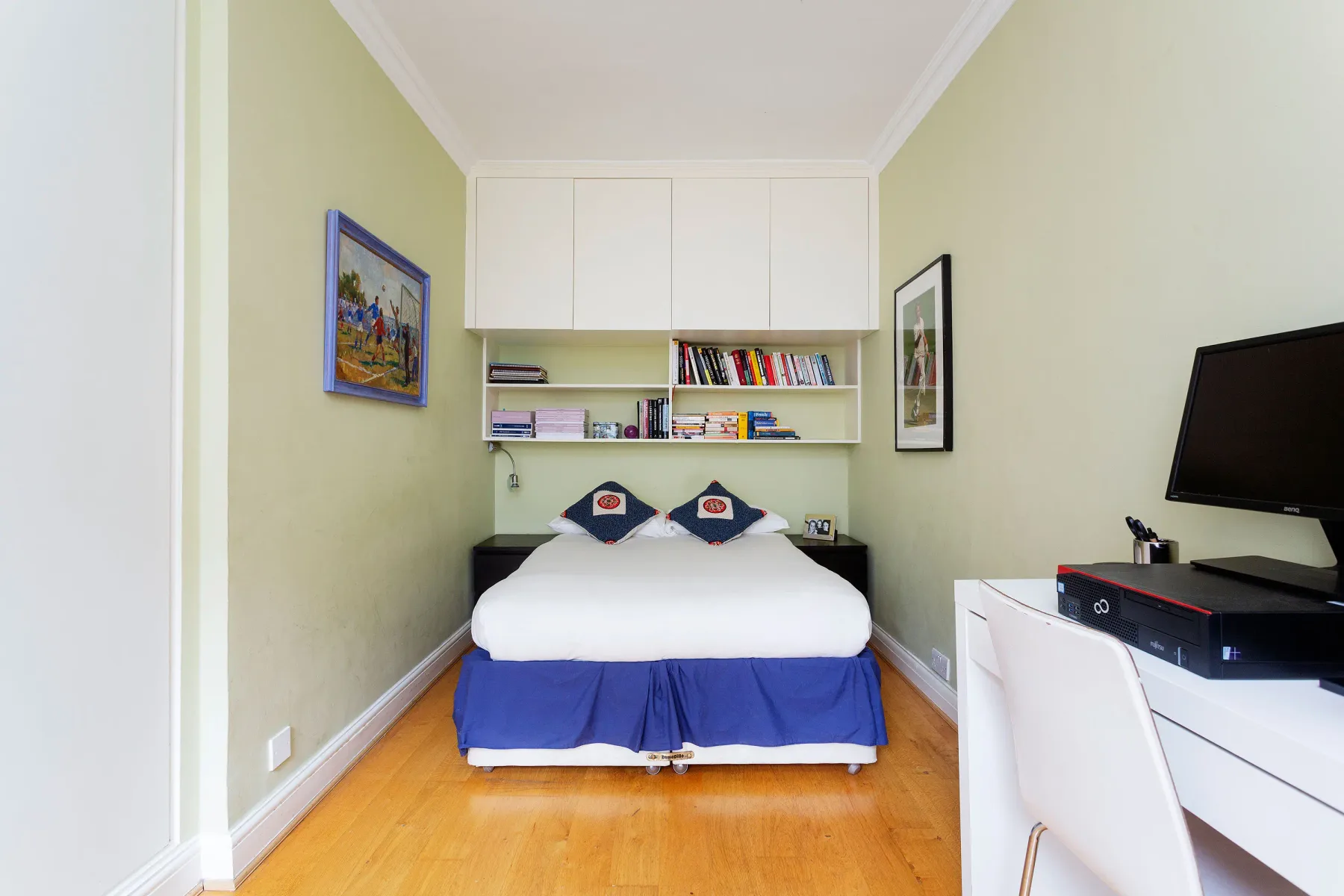 A compact bedroom with a bed beneath built-in shelves and cabinets.
