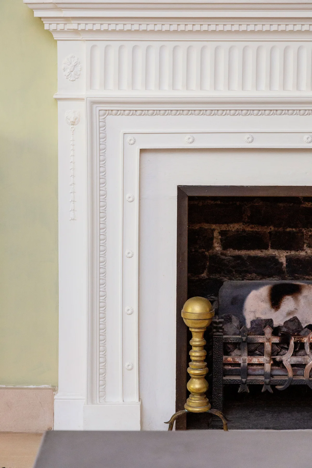 An ornate white fireplace surrounds a dark brick firebox with a brass andirons.