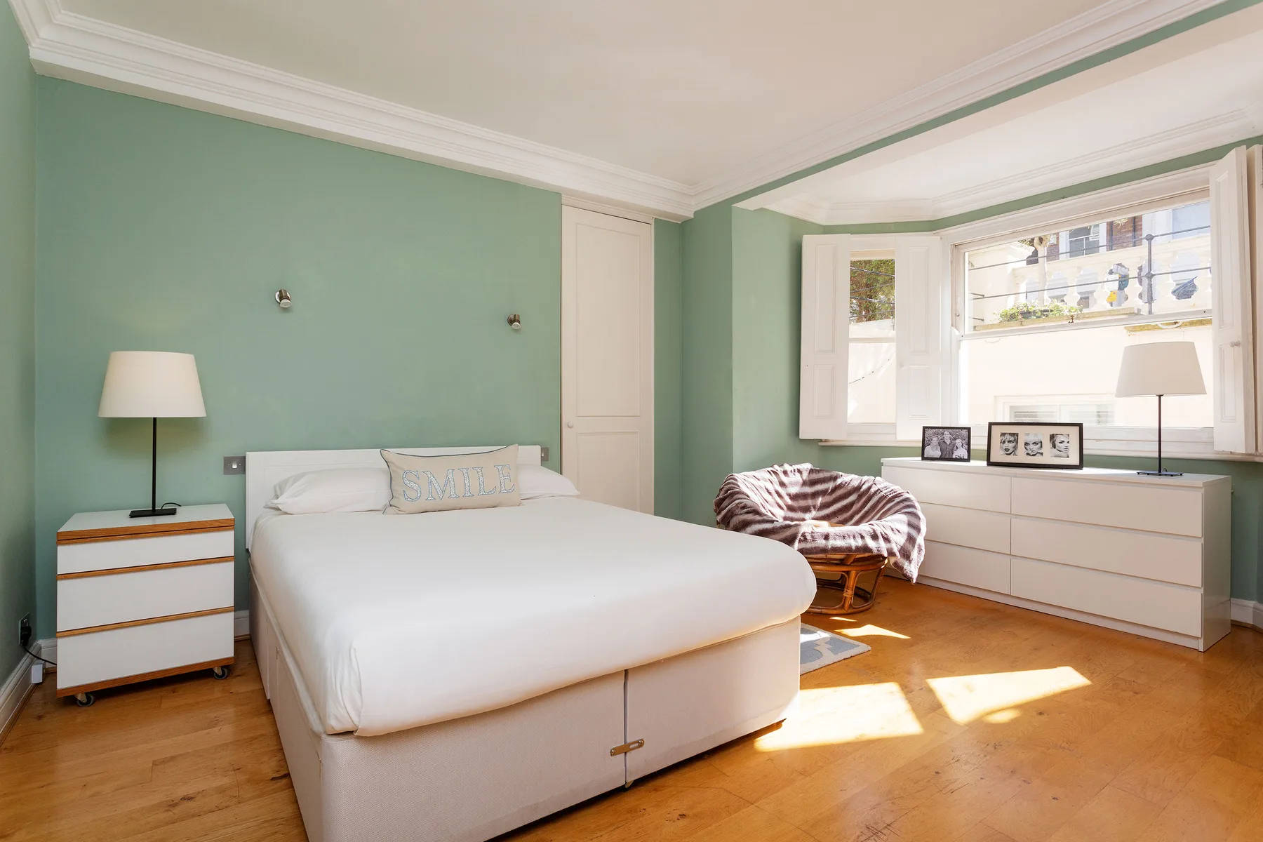 A bright bedroom with a white bed, green walls, and sunlight through the windows.