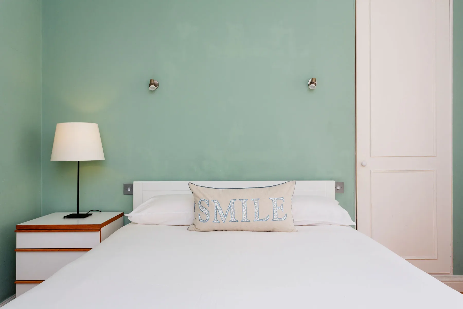 A bedroom with a neatly made bed and a pale green wall.
