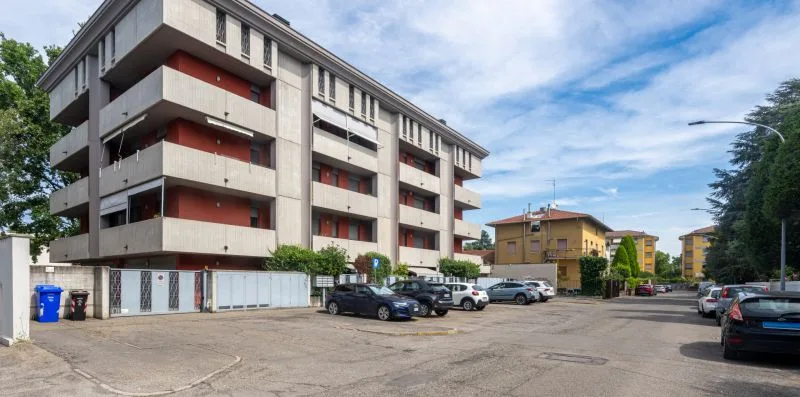 A multi-story apartment building stands beside a paved parking area with cars.