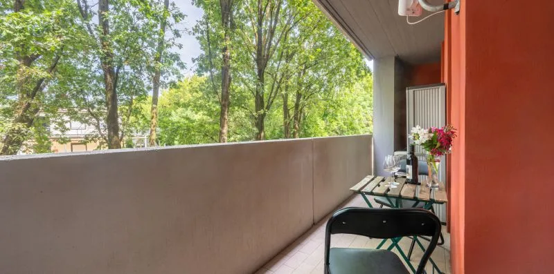 A balcony with a small table and seating overlooks leafy trees.