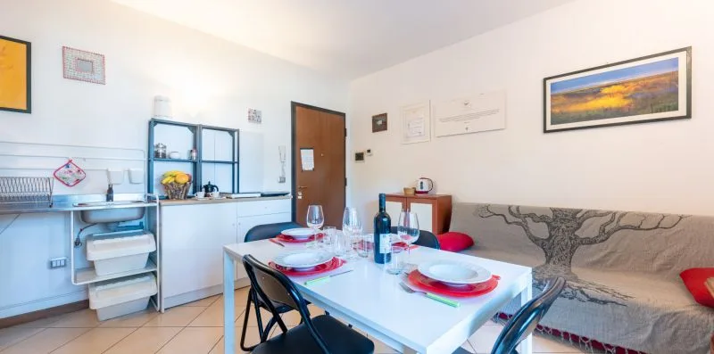 Comedor con la mesa puesta junto a una pequeña cocina y un sofá.