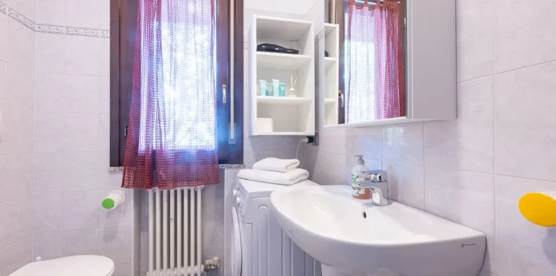 A tiled bathroom with a sink, mirror, and curtained window.