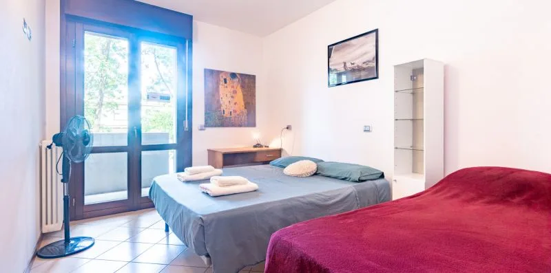 A bright bedroom with two beds beside a large glass door.