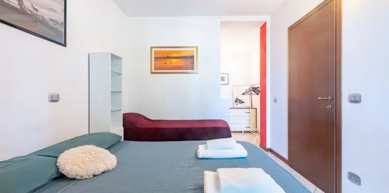 Un dormitorio con una cama, toallas dobladas y una estantería estrecha.