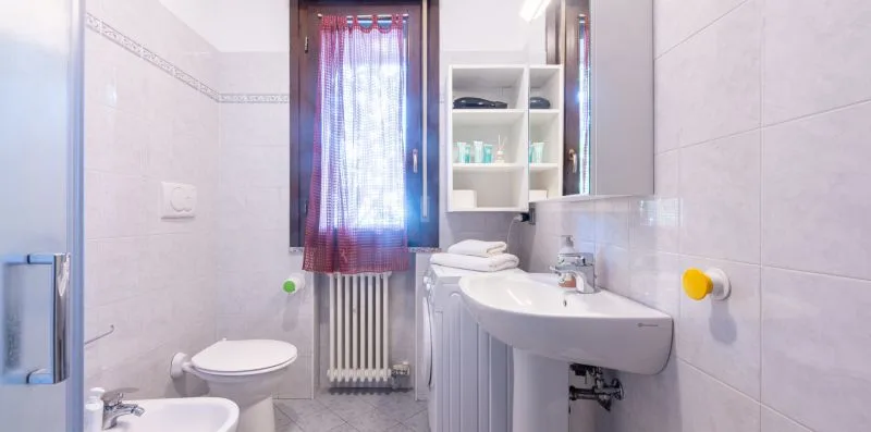 A tiled bathroom with a toilet, bidet, and sink beneath a mirror.