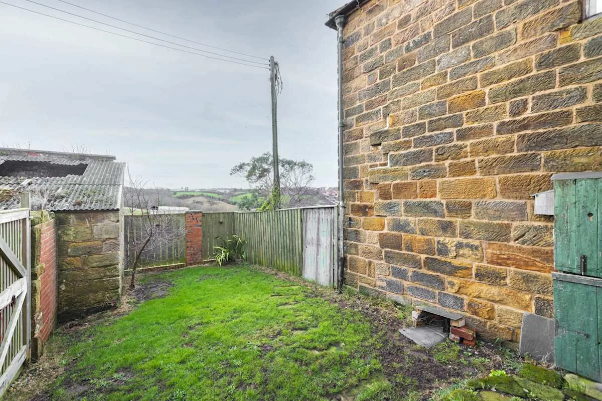 Un pequeño patio exterior con una zona de césped junto a un muro de piedra.