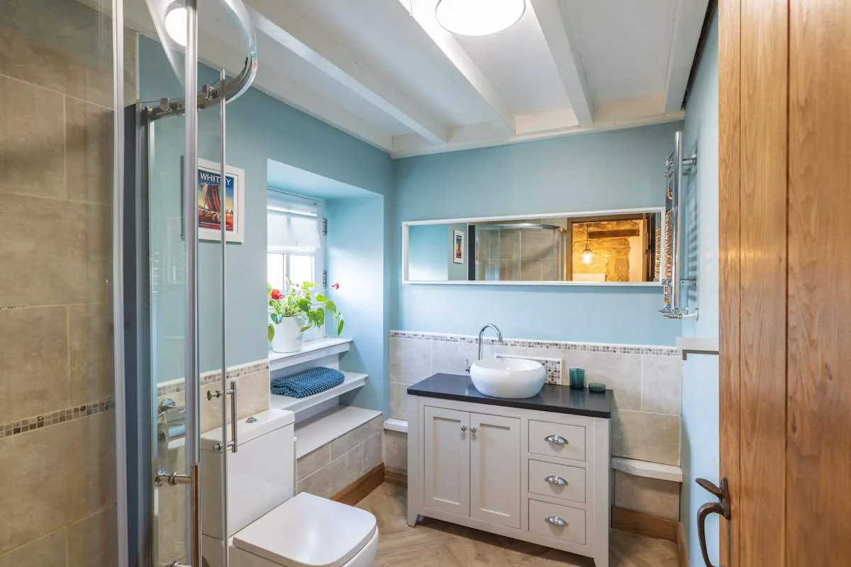 Un baño luminoso con lavabo, espejo y una ventana con plantas.