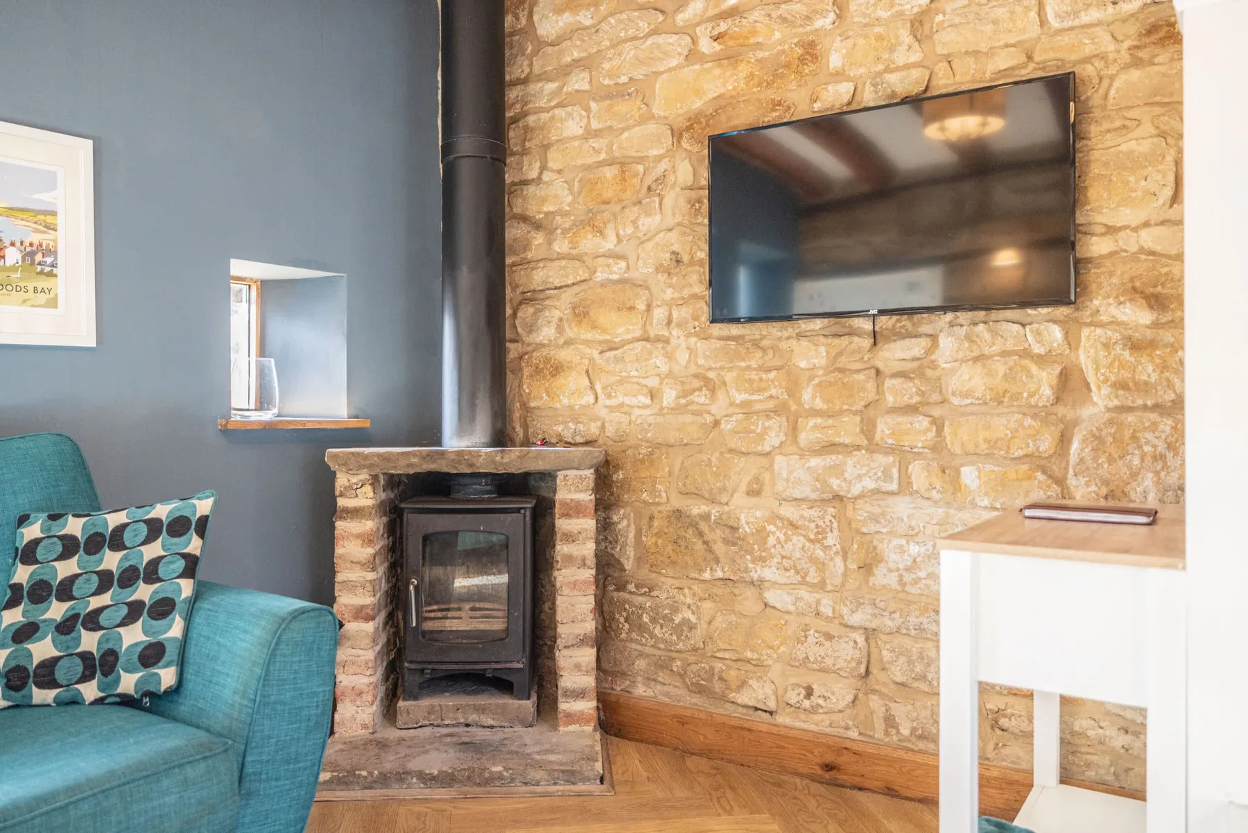 Una sala de estar con un sofá turquesa, una chimenea de piedra y un televisor en la pared.
