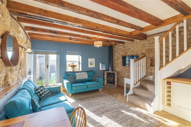A living room with teal seating and exposed wooden ceiling beams.