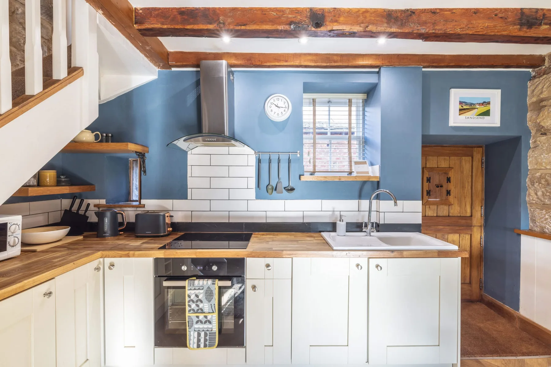 Una cocina luminosa con gabinetes blancos, encimera de madera y paredes azules.