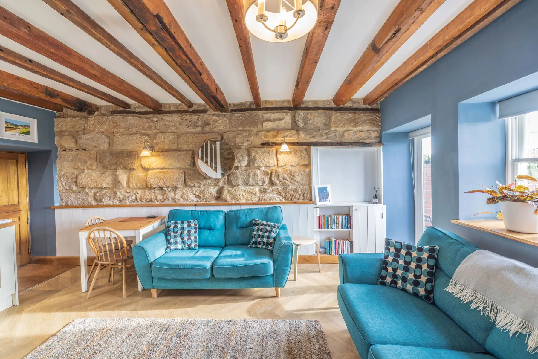 Una sala de estar con asientos turquesa, una pared de piedra y vigas de madera expuestas.