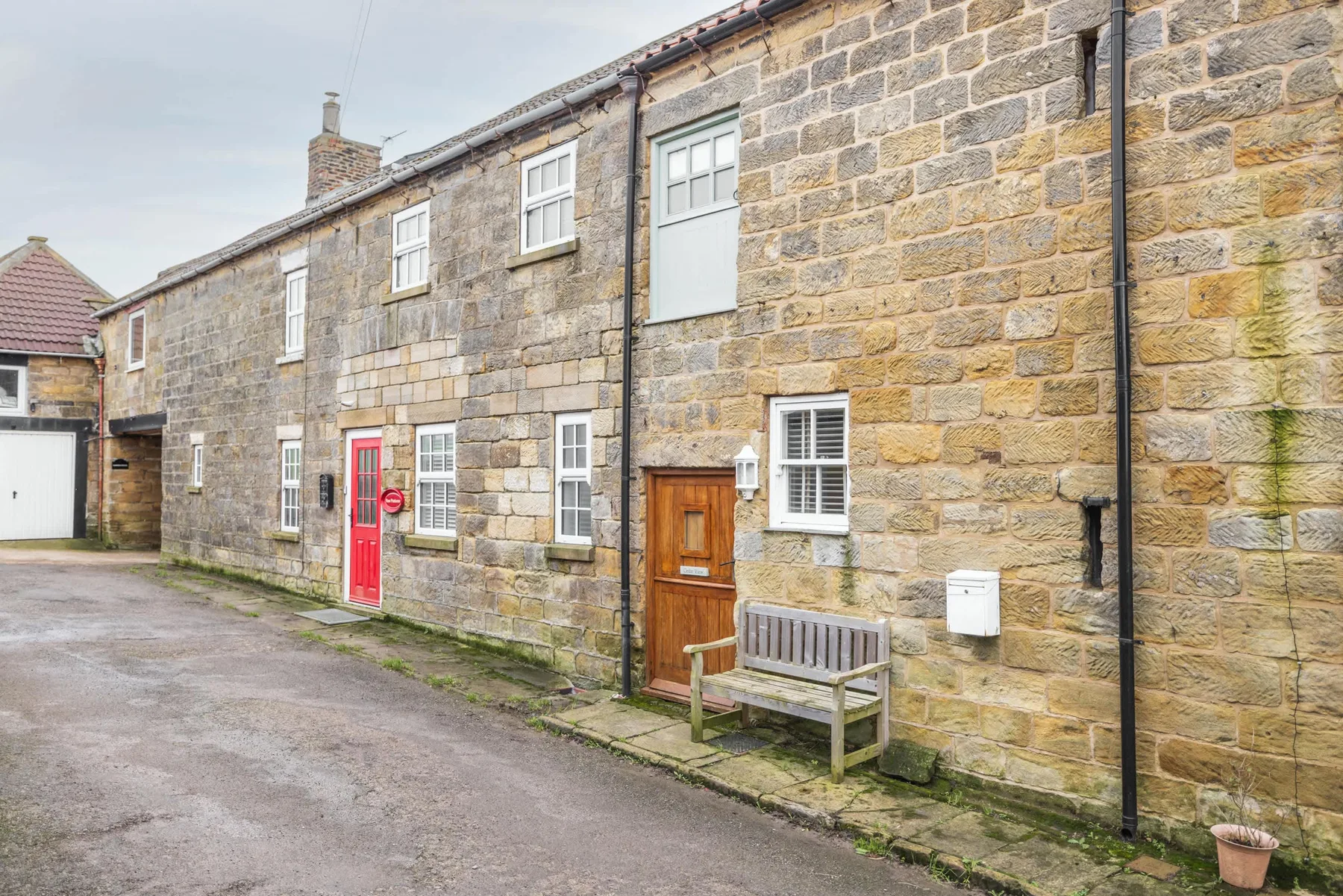 A stone building exterior with a wooden door, red door, and bench along the lane.