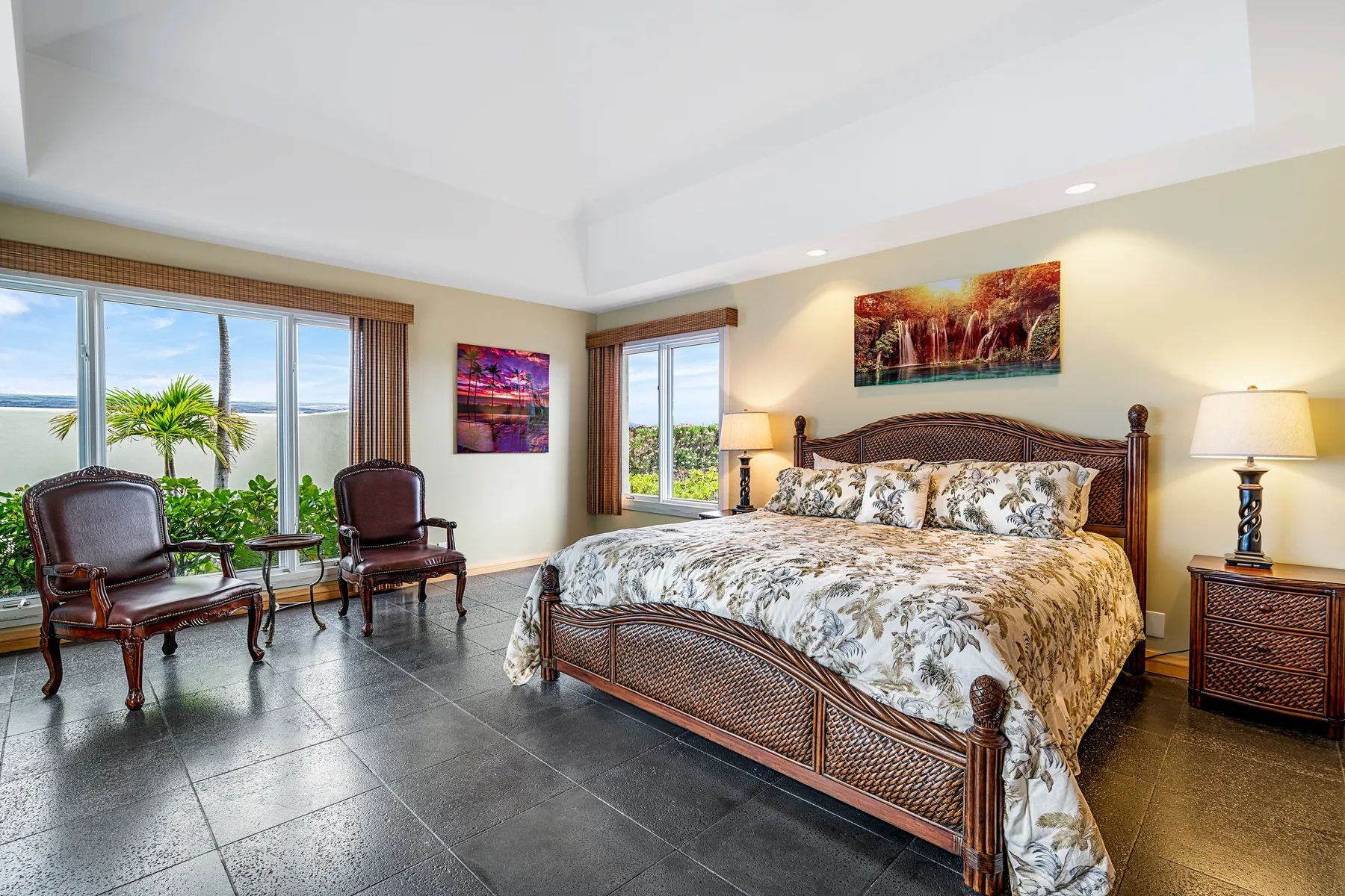 A bedroom with a large bed, armchairs, and windows overlooking greenery and water.